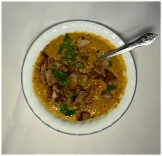 Quebecois-style pea soup. The soup is yellow with shredded ham-hock, garnished with green parsley and specks of black pepper.