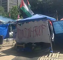 Large banner hanging from a tent in front of the encampment, with the words "injunction-proof" written on it