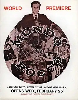 A film flier with the bust of a white shaved man in a jacket and tie over a circular collage of sepia and black photographs of white shaved men, some of them alone, some in couples, most of them naked. The text "MONDO ROCCO" is imposed over the collage. The red text "WORLD PREMIERE" is on the top of the flier. Under the collage, "CHAMPAGNE PARTY · MEET THE STARS · OPENING NIGHT AT 8 P.M.", "OPENS WED., FEBRUARY 25", "EXCLUSIVE AT THE PARK THEATRE ONLY!".