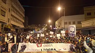 Hirak Rif protests at night, with protesters carrying a banner containing the Republic of the Rif flag and holding Berber flags