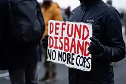 A protest sign with the words "defund / disband / no more cops"