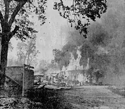 A grainy, black and white newspaper photo of a one-story building completely engulfed in flames