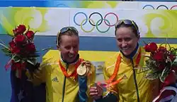 Two women holding bouquets and Olympic medals in their hands