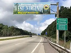 A sign above the highway reads "Welcome to West Virginia—Wild and Wonderful." An adjacent sign reads "Preston County. Certified Business Location."