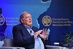 Seiple, from the waist up, sitting down in front of a blue background