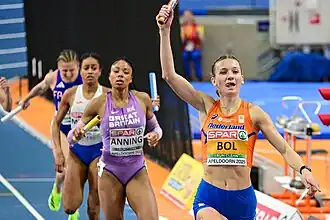 Frontal photo of Femke Bol raising the baton, followed by Amber Anning, Lurdes Gloria Manuel, and Amandine Brossier