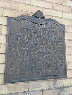 An iron plaque for the Startup Candy Factory building, donated by the Daughters of Utah Pioneers. It is embossed with the following words: Daughters of Utah Pioneers, number 360, erected 1969. Startup Candy Factory. In 1868, William D. Startup brought across the plains the tools of candymaking: scales, iron edging bars, drop machine, shears, and hooks. After pursuing his profession in Salt Lake City, he moved to Provo and built the first candy factory in 1875. Following his death, 1878, his widow Hagar continued the business for ten years. In 1895 her sons William, Walter, and George became owners. The original machinery is preserved at the present factory. At the bottom is signed "Center Utah County."