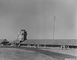 Black and white photograph of a building with multiple people standing in front of it, and the American flag flying