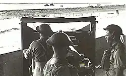 Gunners at 4.7-inch (120 mm) gun watching vessels at river mouth. 1943.[gallery 16]