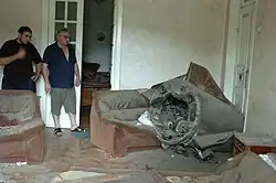 Two men looking at a missile lying across a sofa