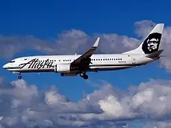 Left side view of an aircraft on final approach, with partly cloudy skies in the background.
