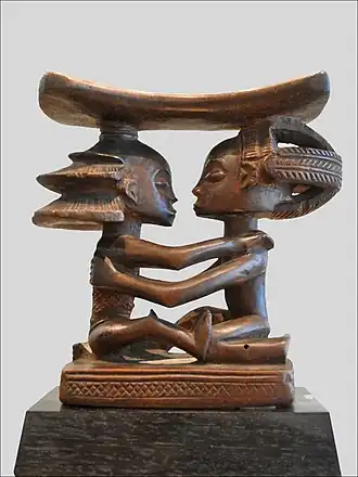 Headrest; 19th century; wood; height: 18.5 cm (7.3 in), width: 19 cm (7.5 in), thickness: 8 cm (3.1 in); Musée du quai Branly (Paris). This headrest presents 19th century Luba hairstyles, as well as the long limbs, bent-back legs, cylindrical torso and dynamic pose typical of the artist who made it.