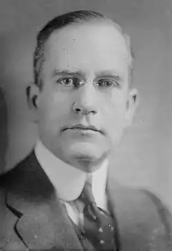 Black and white portrait photograph of Shaw from neck up wearing a suit jacket, necktie, and glasses