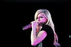 Avril Lavigne wearing a black gown and singing in to a microphone.