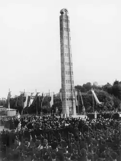 Photo of the ceremonial unveiling of the obelisk of Axum in Rome; a large crowd of people, including Blackshirts with rifles, surround it.