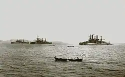 A black and white shot of three large ships near a hill-like background, with several small skiffs in the foreground