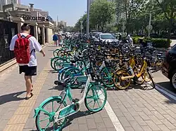 a man waks by teal and yellow bicycles along a street in Beijing