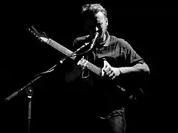 Howard playing an electric guitar while singing into a microphone onstage