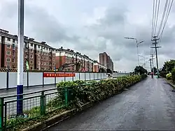 A fenced area runs diagonally across a picture, with buildings behind it.
