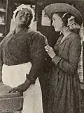 ZaSu Pitts in a wide-brimmed hat standing next to an unidentified black actress in a maid's cap