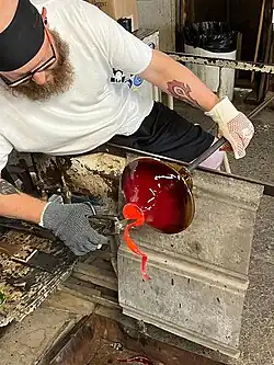 man trimming red hot glassware