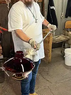 man holding finished, but still hot, glassware with stick