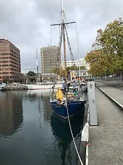 blue boat on a waterfront with some buildings as background and another white boat.