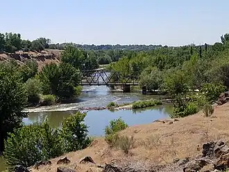 A river flows under a steel bridge through a wooded area