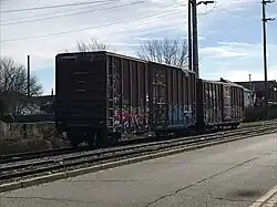 Two boxcars on a siding, adjacent to a second track and then a roadway.