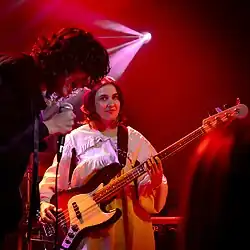 Two musicians, one singing into a microphone and another behind him with a bass guitar.