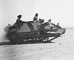 A tracked military vehicle moves across the desert