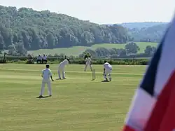A Union Flag in the foreground and a cricket match with English countryside in the background