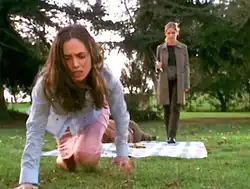 In a park, a terrified Faith crawls towards the camera, the body of the dead Mayor lays behind her on a picnic blanket, as Buffy approaches menacingly holding a knife.