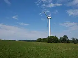 Wind turbine in open field, with turbines on the ridgeline in the background as well.