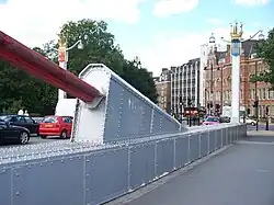 End of a large red suspension cable, attached to a protrusion atop the side of the bridge deck.