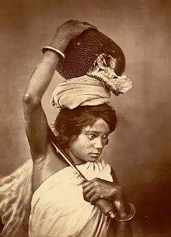 A Kochh Mandai woman of east Bengal (present-day Bangladesh) shown with a broad-bladed agricultural knife and carrying a freshly harvested jackfruit (1860)