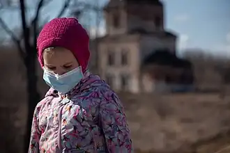 Young girl looking down, wearing a with a pink beanie, floral puffer and a surgical mask