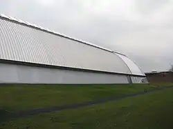 Picture of the exterior of a grey building. The building is a semi-circle made of corrugated metal.