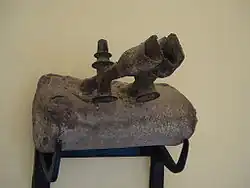 a block with two dull, dark gray metal spouts coming from the top. The spouts are chipped and very old-looking.