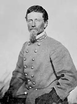 Black and white photo of a man with dark hair and a graying beard. He wears a double-breasted gray uniform with three general's stars on the collar.