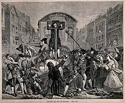 Daniel Defoe stands in a pillory on a high platform. Around him is a thick crowd of people, some of whom are waving their hats and trying to give him flowers. Soldiers around the platform attempt to hold them back.