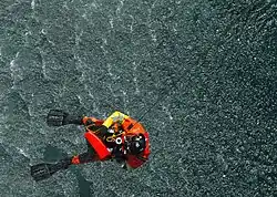 A rescue swimmer from Coast Guard Air Station Cape Cod, Massachusetts, is hoisted back into an HH-60 Jayhawk after retrieving a rescue training dummy.