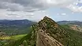 A hiker stands on a steeply slanted rock formation high up in the mountains looking out at the view.