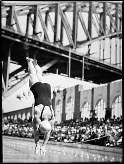 Black and white photo of a diver at the North Sydney Olympic Pool. The Sydney Harbour Bridge is in the background.