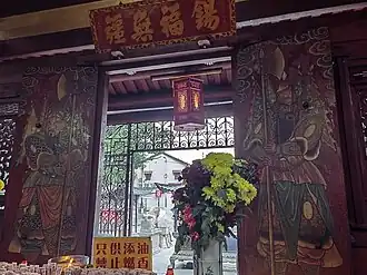 Traditional door guardian paintings (Menshen 门神) at the entrance, with a wooden plaque inscribed “锡福无疆” (Limitless Blessings and Harmony).