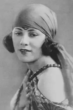 A young white woman with dark bobbed hair, wearing a headscarf and a costume with bare shoulders