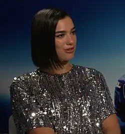 Dua Lipa wearing a glittery dress against a blue background