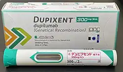 Photo of a Dupixent (dupilumab) 300mg/2mL auto-injector pen and accompanying packaging. The pen is labeled in Japanese.