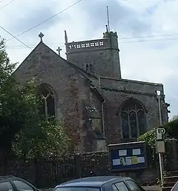 Red and grey stone building with arched windows and triangular roof. Behind is a small square tower