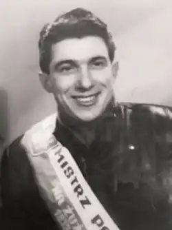 alt=black-and-white photograph of a man sporting a leather jacket and a sash that reads (in Polish): "MISTRZ POLSKI NA ŻUŻLU 1952", which translates to "Polish Champion in Speedway 1952"
